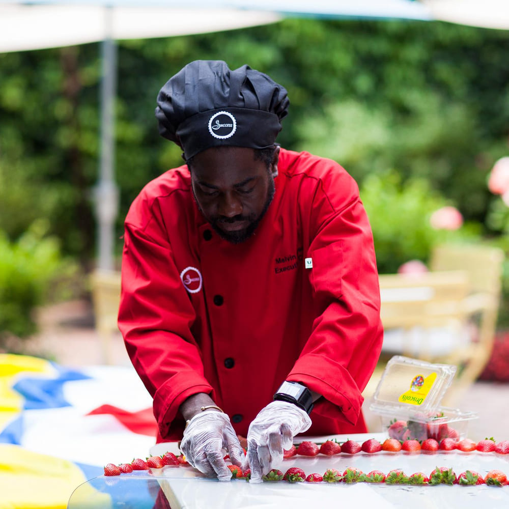 Chef Melvin Myers in a red chef's coat arranging strawberries at an outdoor event.